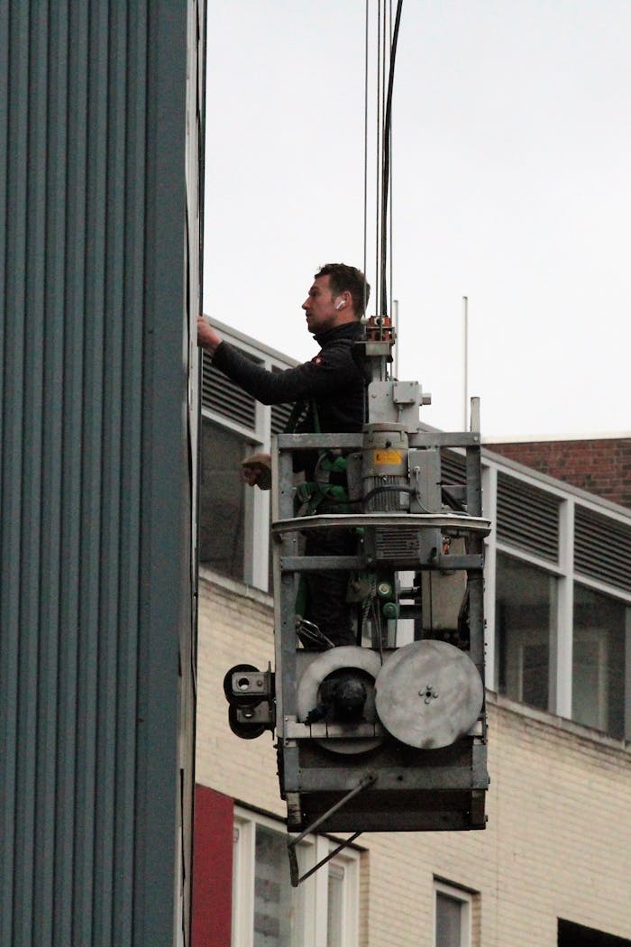 A man repairs a building facade from a suspended platform in an urban setting.