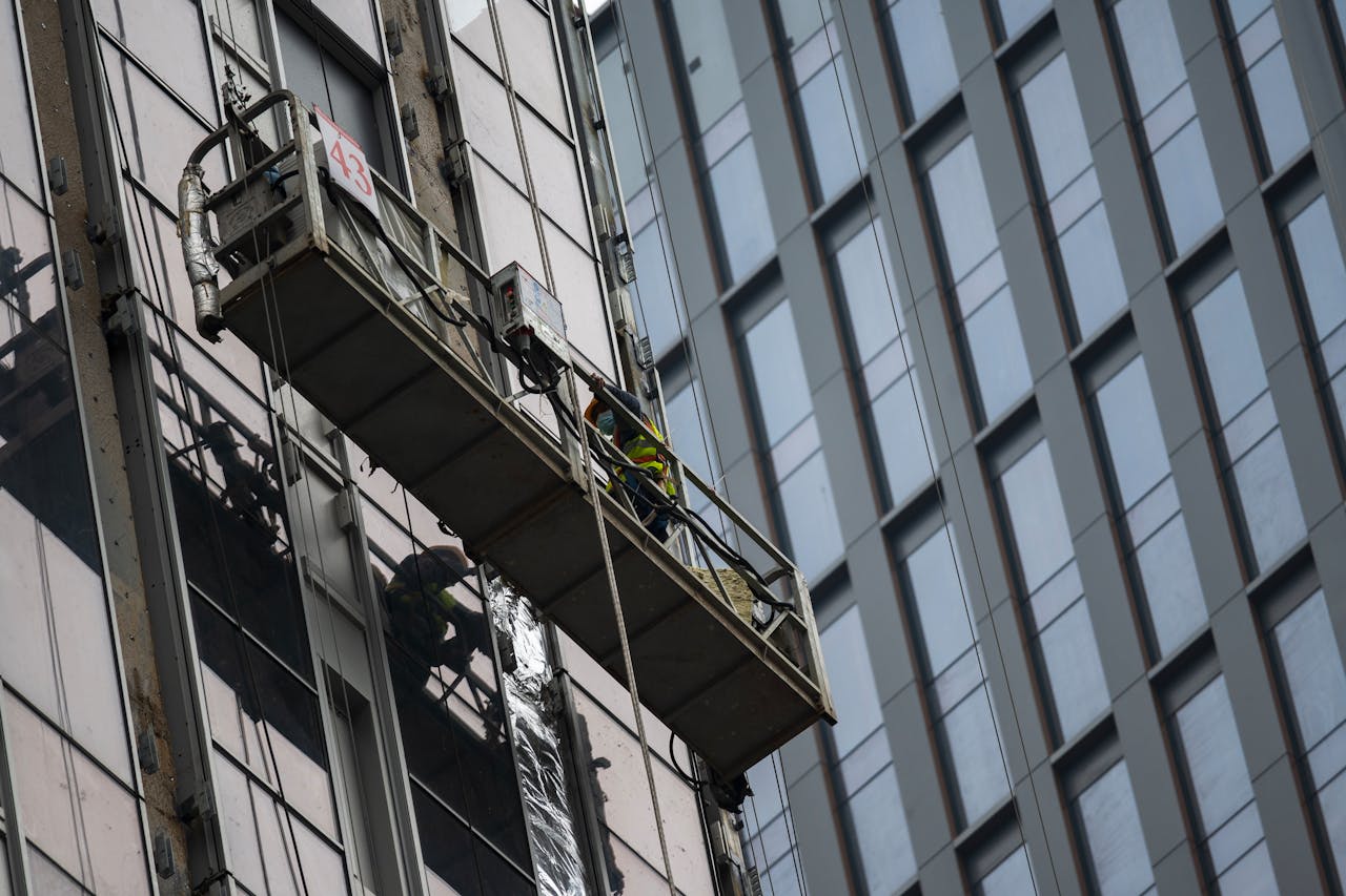 services-04 Workers on a suspended platform cleaning windows of a high-rise building in a cityscape.